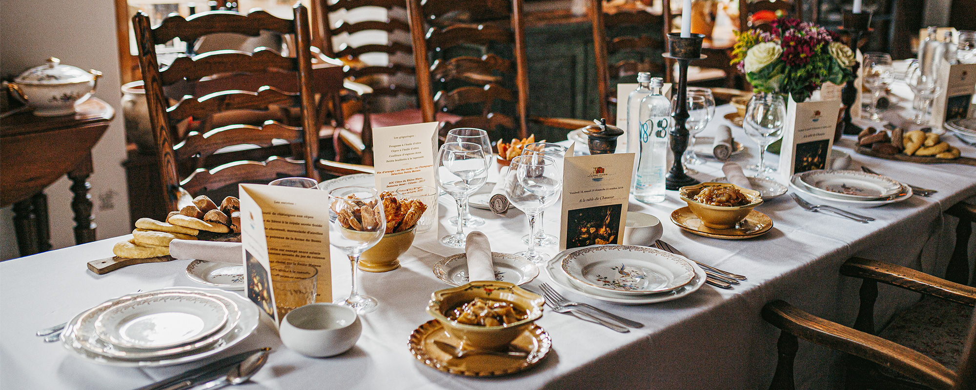 une grande table à manger, avec une belle nappe blanche une grande table à manger, avec une belle nappe blanche, des chaises ancienne en bois viennes accentué ce sentiment de bien être dans un espace chaleureux